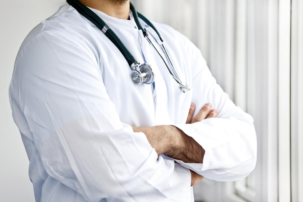 Arzt mit verschränkten Armen in weißem Kittel mit Stethoskop um den Hals
