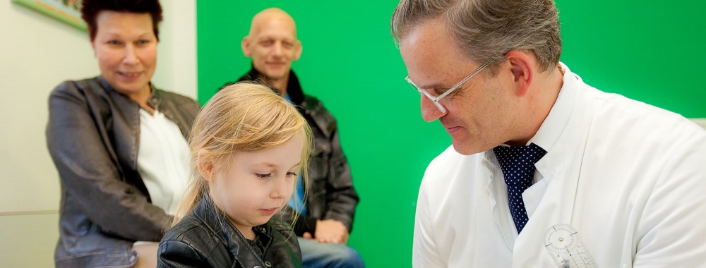 Oberarzt Dr. Jokuszies untersucht ein kleines Mädchen. Die Eltern sind im Hintergrund zu sehen.