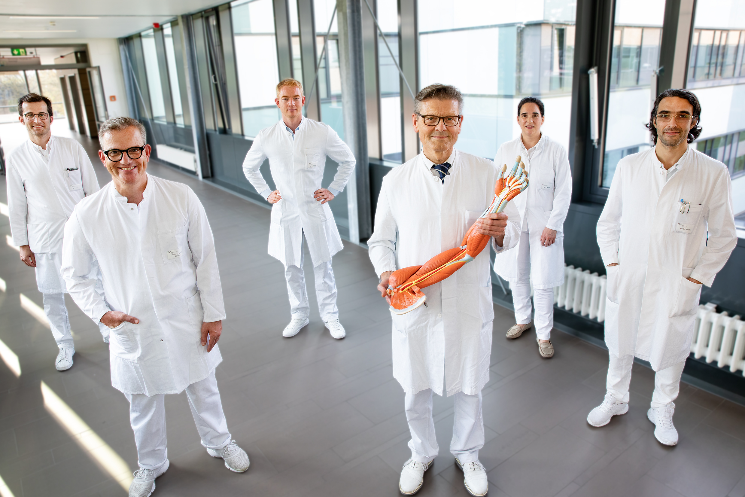 Gruppenbild der Oberärzte der Klinik mit Prof. Vogt, welcher ein Anschauungsmodell eines Armes mit Hand hoch hält.