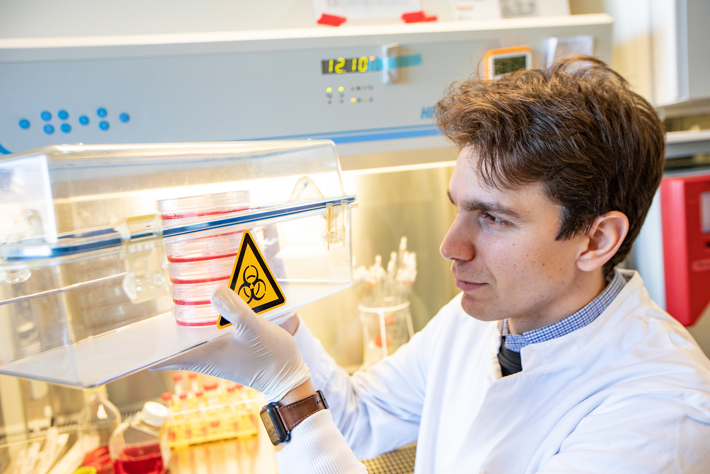 A young scientist sits at a workbench in the laboratory and shows cell cultures.