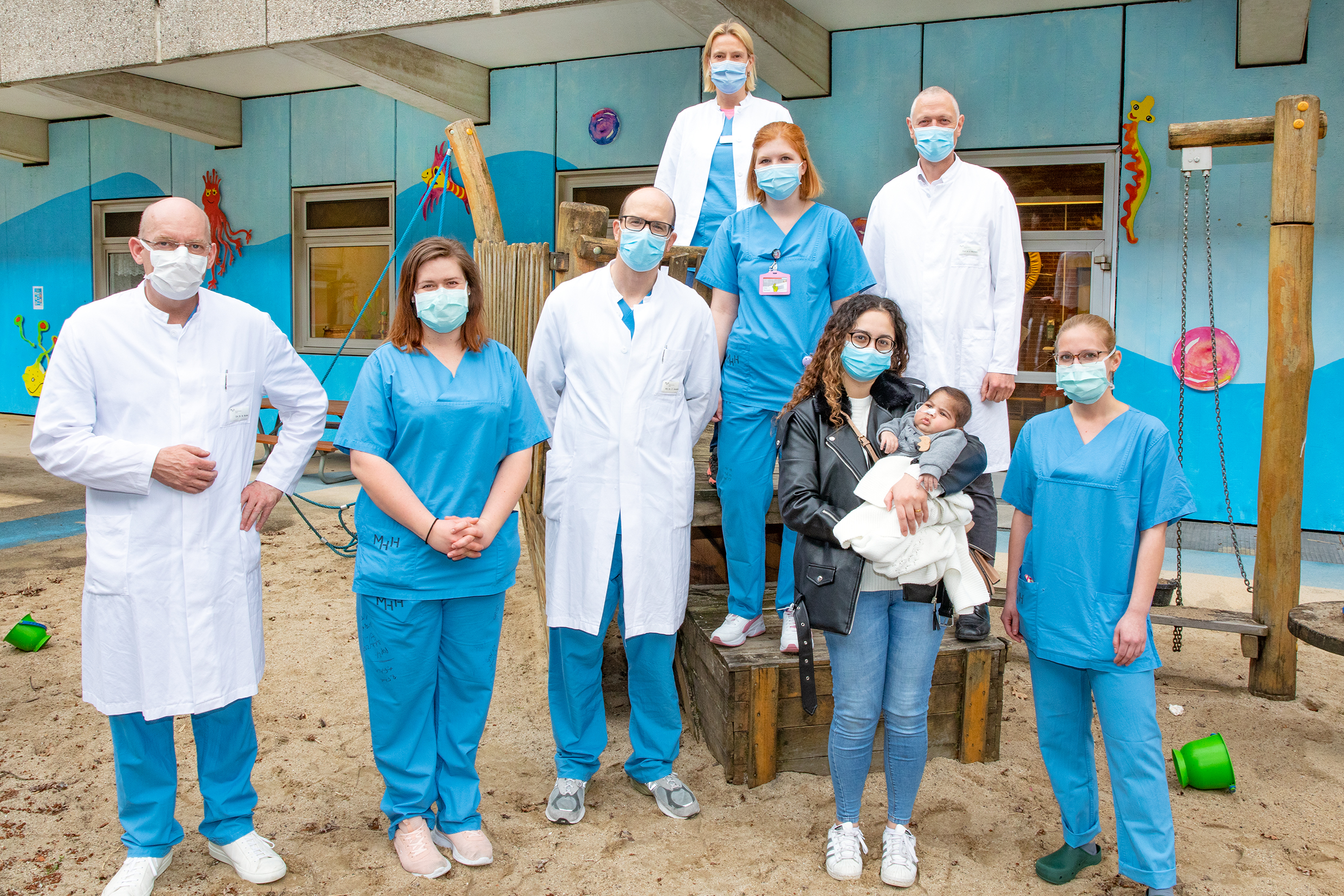 Adam mit seiner Mutter und das Ärzte- und Pflege-Team haben sich auf einem Spielgerät im Innenhof der Kinderklinik aufgestellt.. Copyright: Karin Kaiser/MHH 