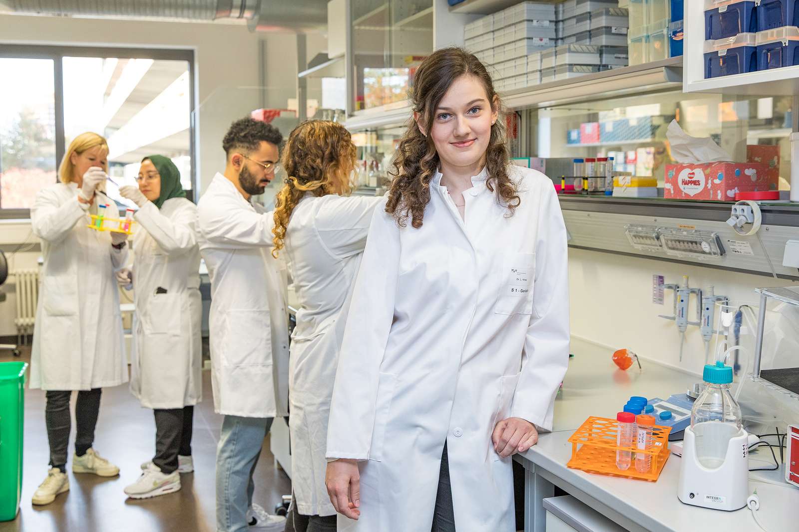 The young doctor Dr Laura Hinze stands in her laboratory with her research group.