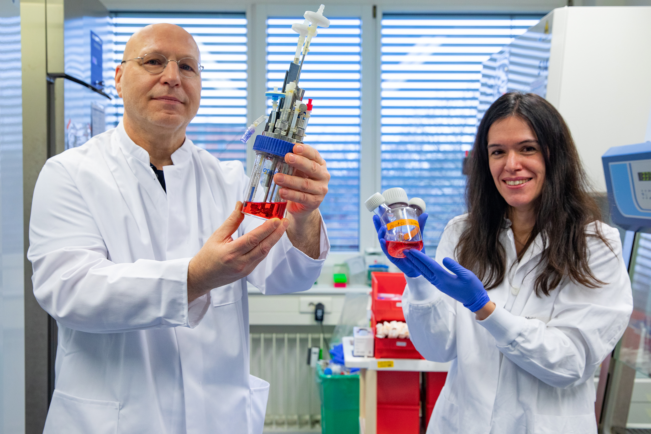 Professorin Dr. Constanca Figueiredo und Professor Dr. Rainer Blasczyk stehen in einem Labor des Instituts für Transfusionsmedizin und Transplantat Engineering und zeigen Bioreaktoren zur Blutzellgewinnung.