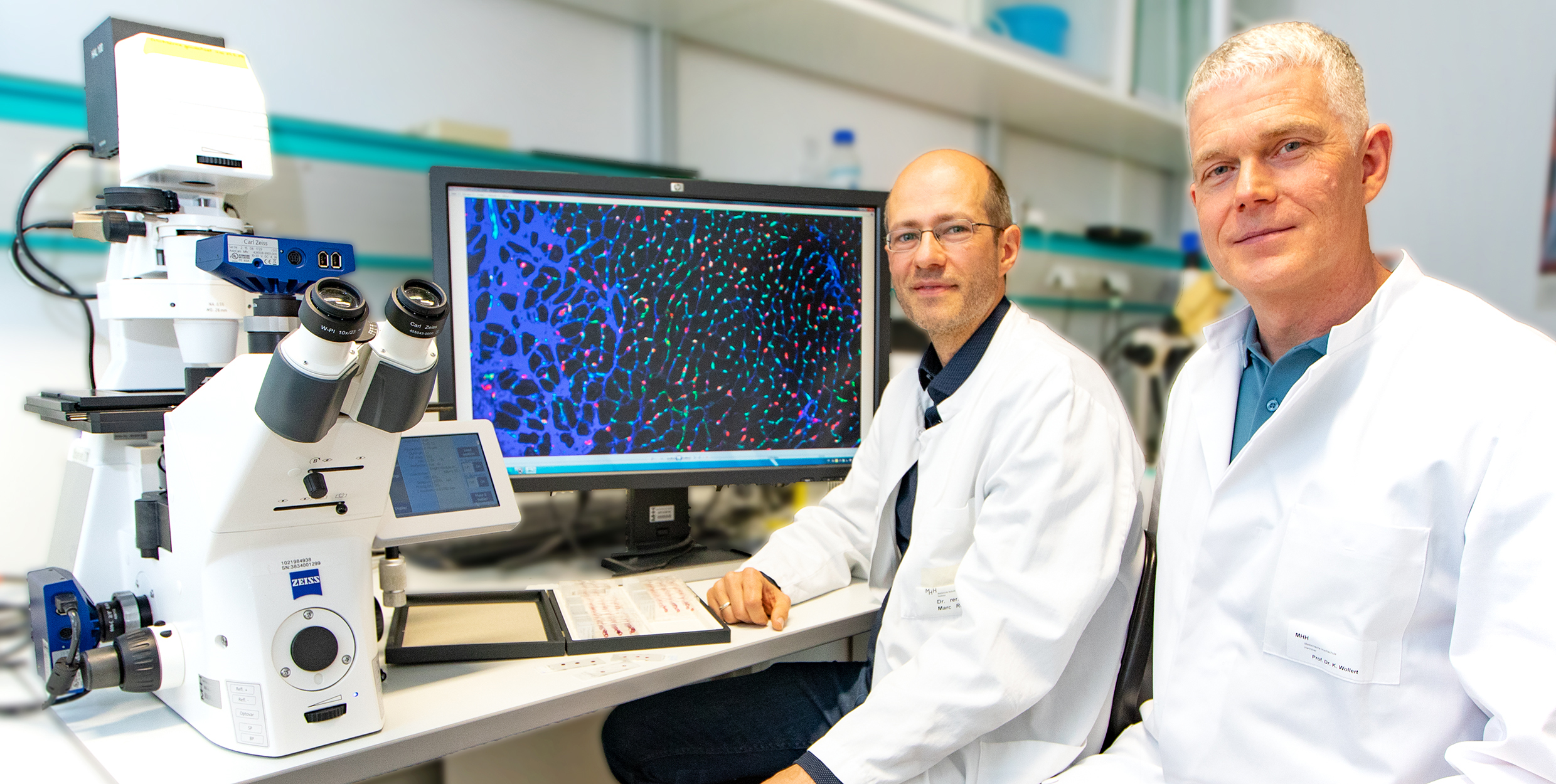 Dr Marc Reboll and Professor Kai Wollert sit in front of a fluorescence microscope in the MHH Department of Cardiology and Angiology