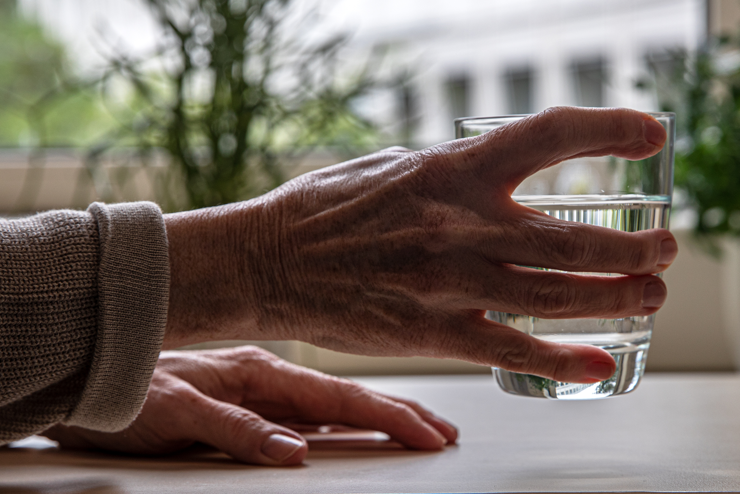 Eine ältere Hand, die ein Wasserglas hält.
