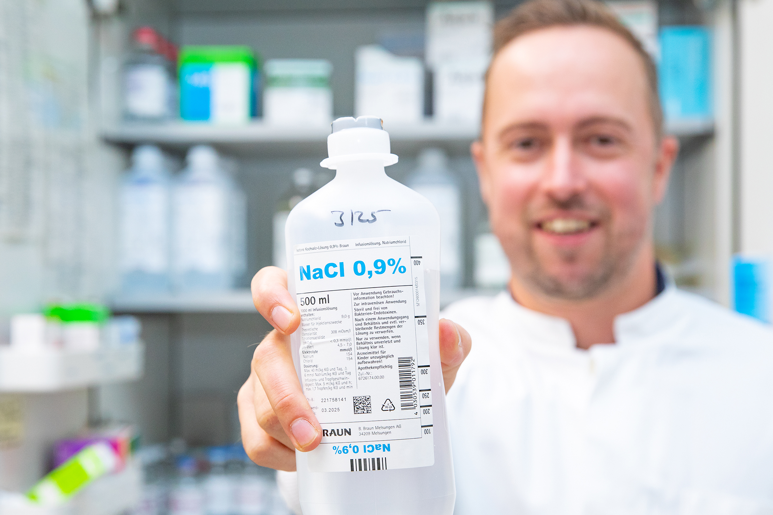 A bottle of sodium chloride infusion solution can be seen being pointed towards the camera by Professor Lachmann. Professor Lachmann aims to revolutionise the safety of drugs administered parenterally by injection