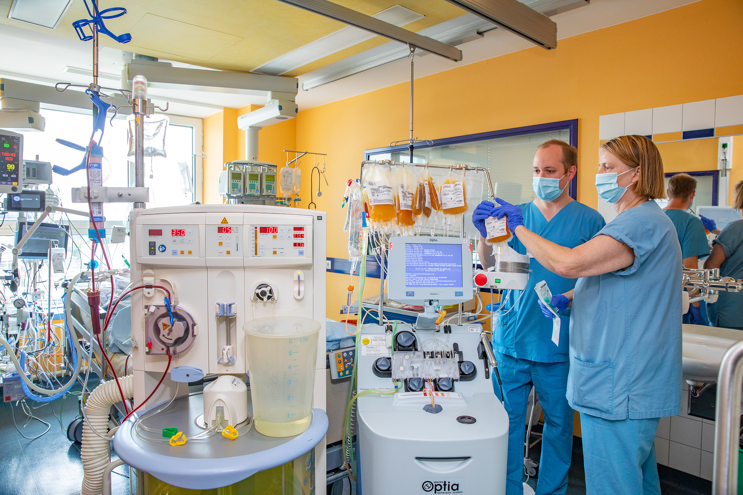 A doctor and a specialist nurse stand at a plasma exchange device in a patient room.