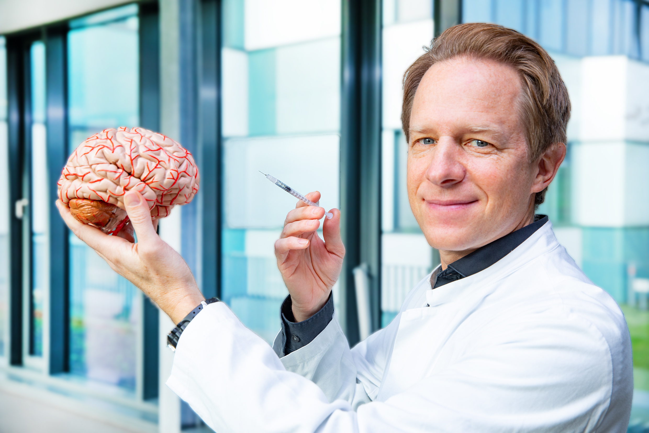 Professor Dr. Tillmann Krüger hält das Modell eines menschlichen Gehirns und eine Spritze in den Händen.