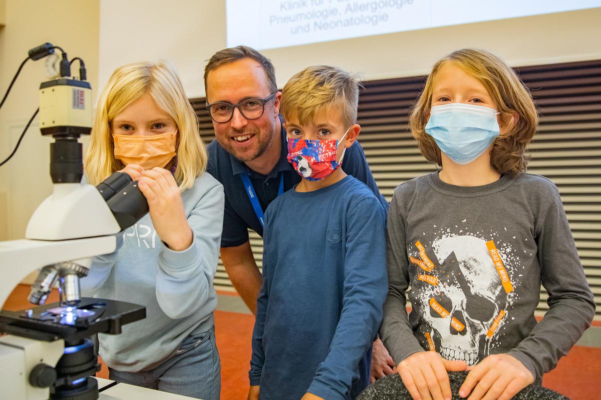 Professor Dr. Nico Lachmann steht zwischen 3 Kindern im Hörsaal.