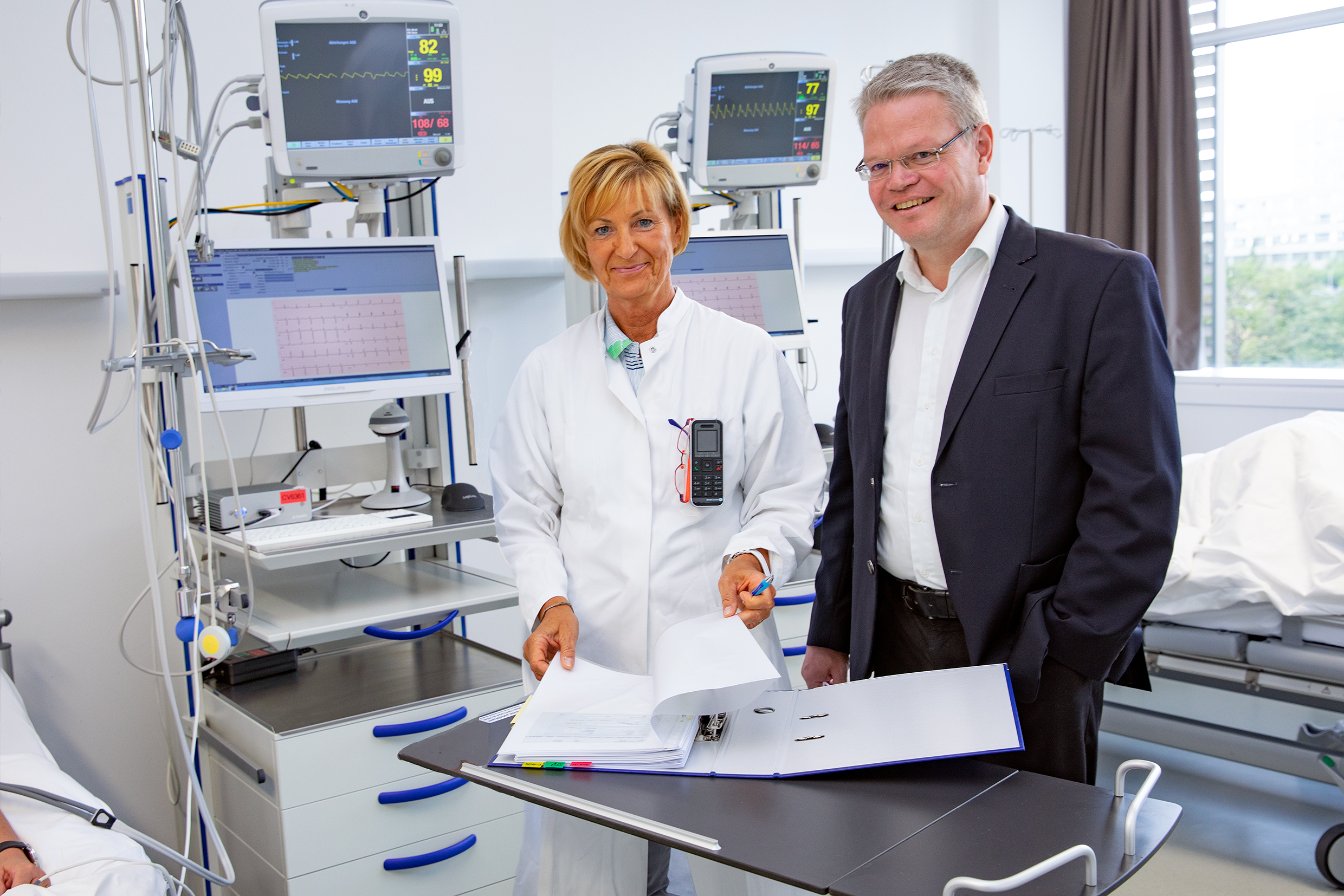 Professor Dr. Christoph Schindler und Carola Westenberg stehen in einem Patientenzimmer des Zentrums für klinische Studien.