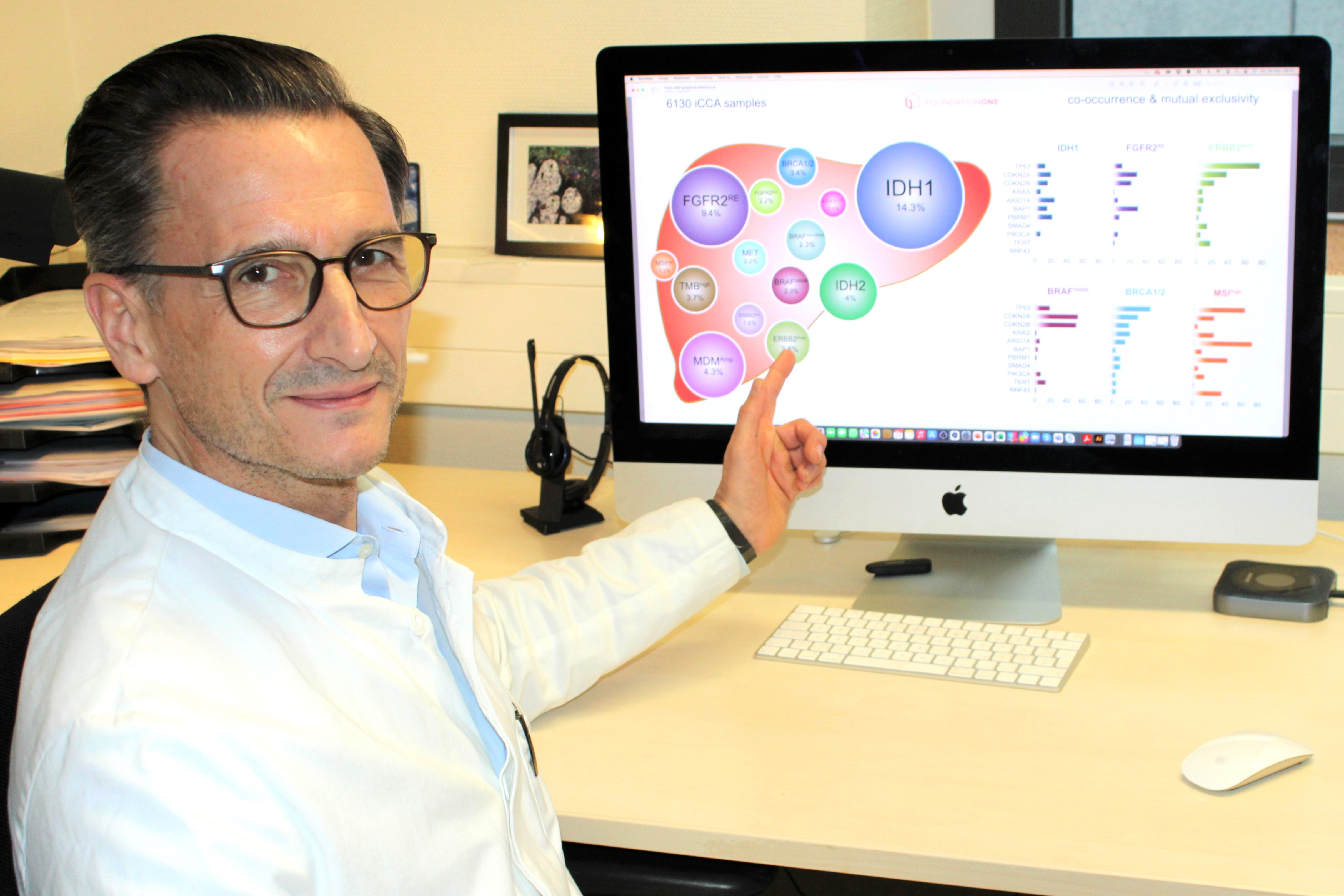 Copyright: Maike Isfort /MHH Professor Dr. Arndt Vogel vor einem PC auf dem die Grafik von genetischen Veränderungen von Gallenwegkrebs dargestellt wird.