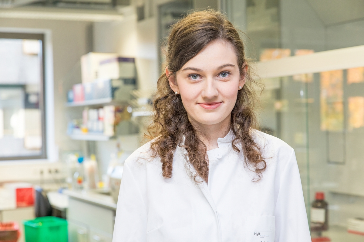 Laura Hinze stands in an MHH laboratory and smiles at the camera