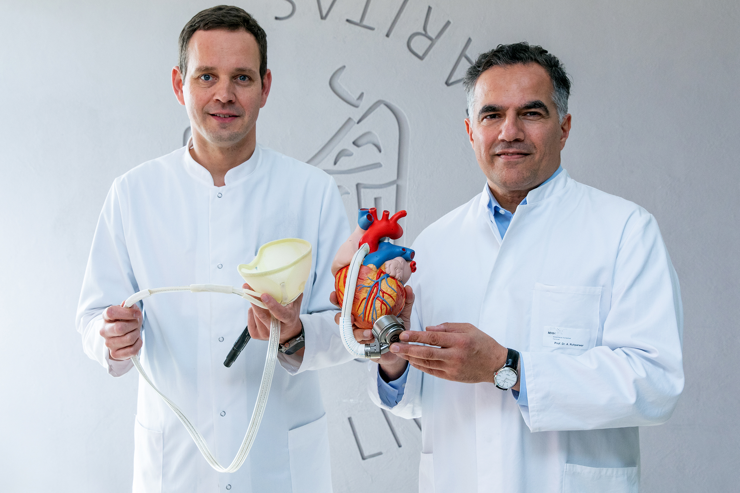 Dr Schmack is holding the plastic bag of the reBEAT system in his hand, while Professor Ruhparwar shows a heart model with an implanted conventional left ventricular assist device.