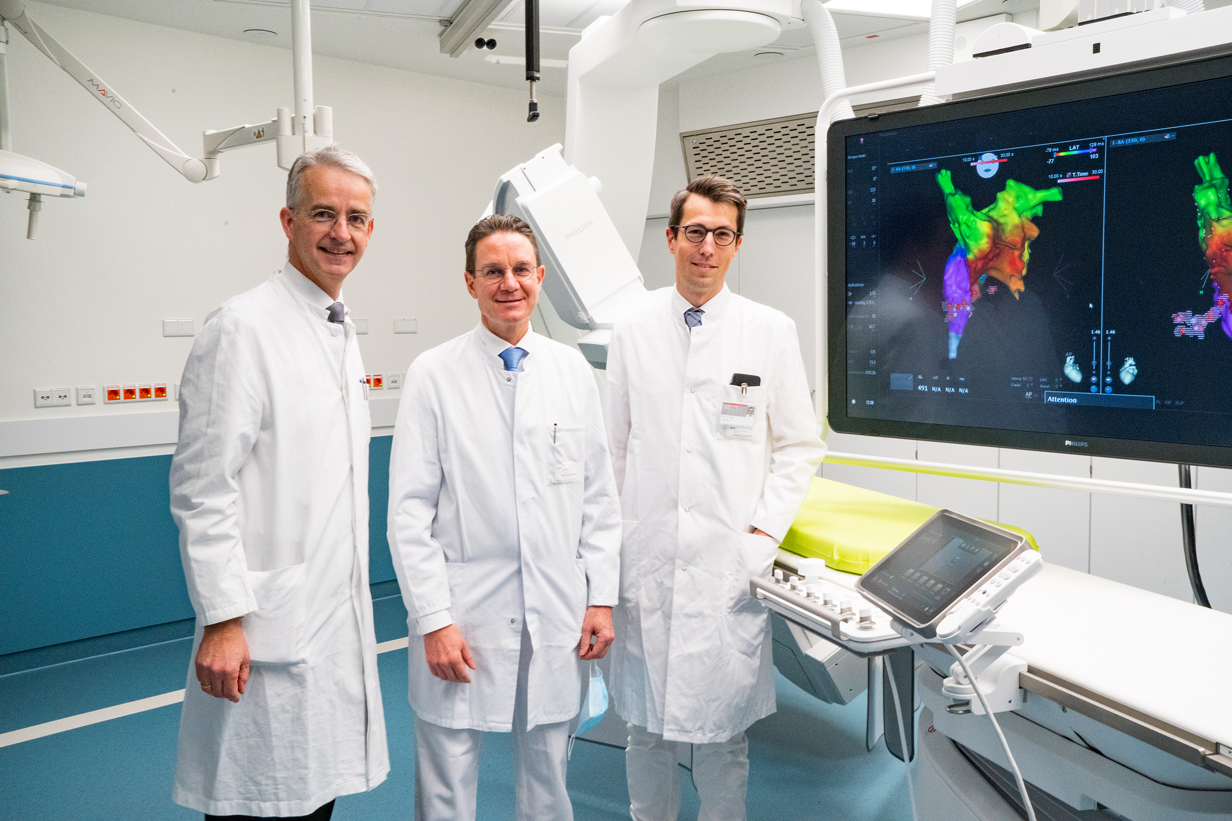 Professor Dr Frank Lammert, Vice-President of the MHH, Professor Dr Johann Bauersachs, Director of the Department of Cardiology and Angiology, and Professor Dr David Duncker, Head of the Hannover Heart Rhythm Centre, stand in the new electrophysiology laboratory. In the background are screens with colour 3-D images of the heart.