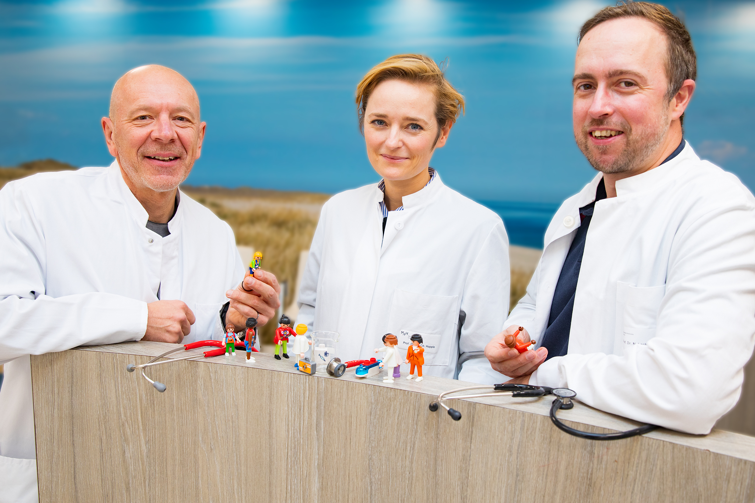 The photo shows Professor Dr Nico Lachmann, spokesperson for the new training programme nextGENERATION, with co-spokespersons Professor Dr Christine Happle (centre) and Dr Robert Zweigerdt (left). They are standing behind a balustrade on which small figures can be seen that are meant to symbolise people in the hospital, as well as small objects from the laboratory. This is meant to represent the networking of research and clinic, which this new training course strongly advocates