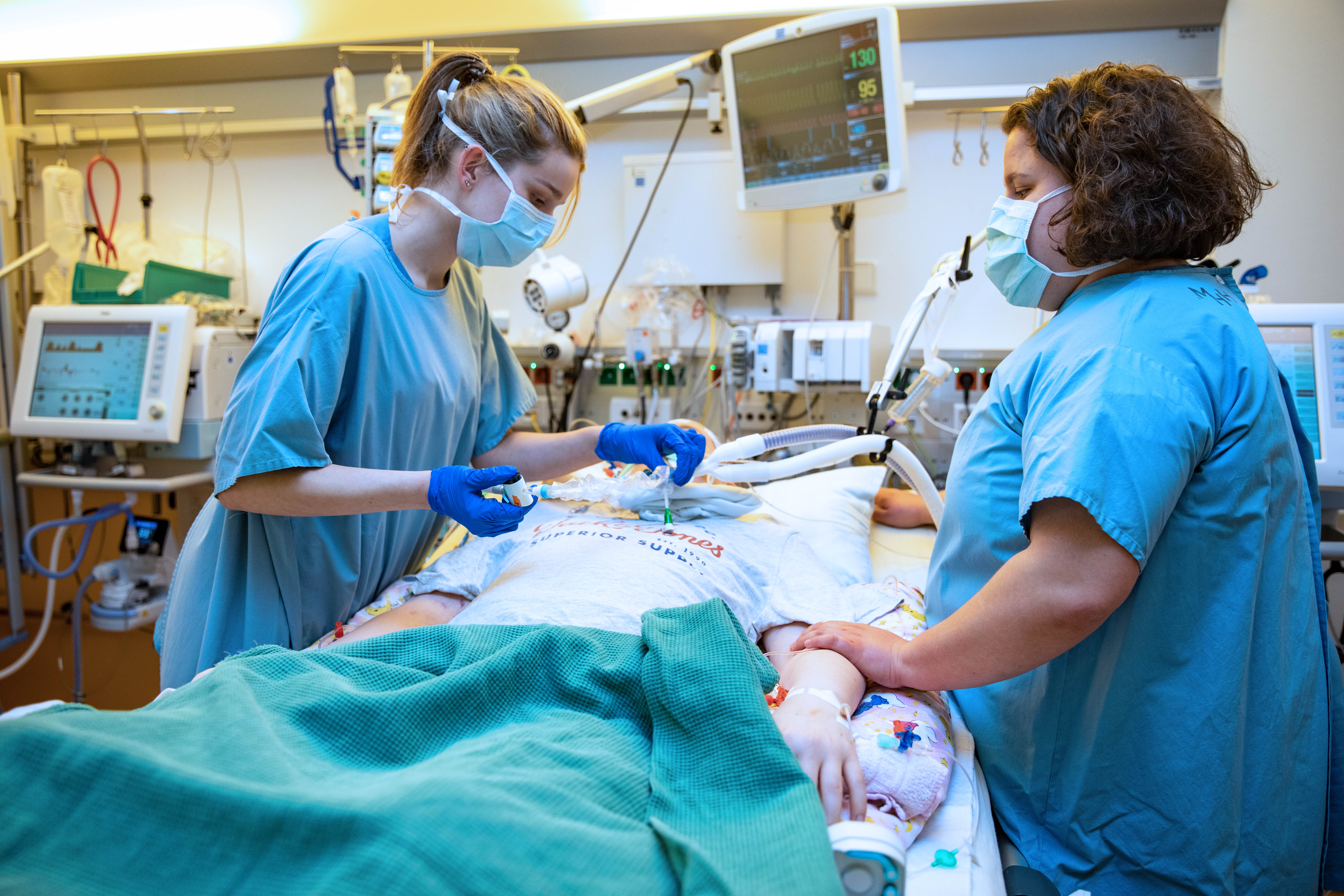 Two nurses in an intensive care unit at the bedside of a patient.