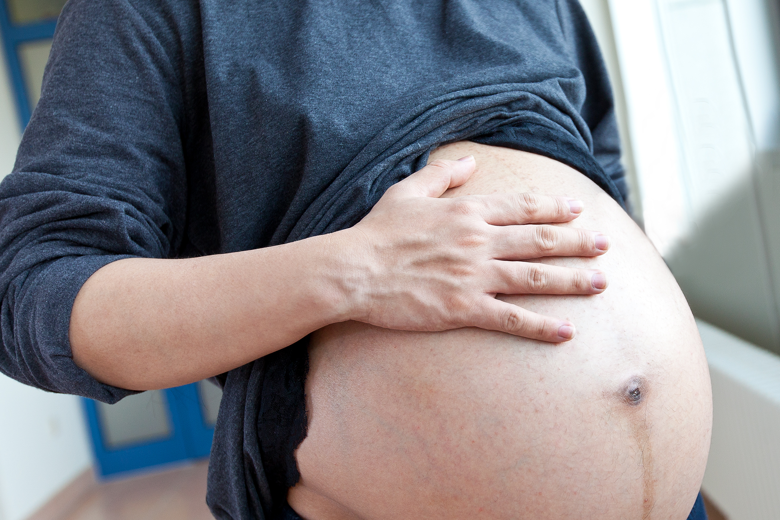 Eine schwangere Frau berührt ihren Bauch.