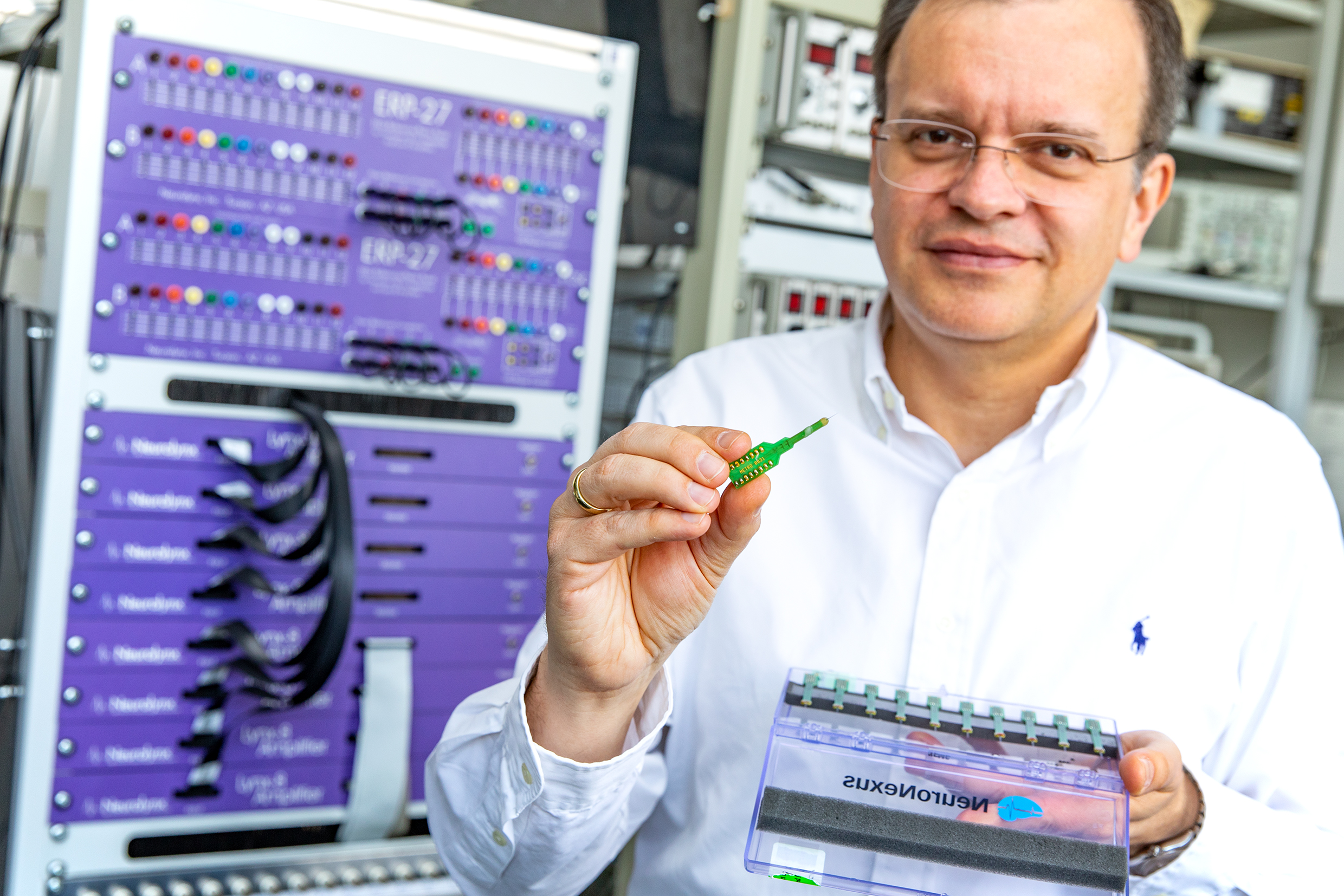 Professor Dr. Andrej Kral stands with a multi-electrode array in his hand in front of an amplifier for brain wave measurement.
