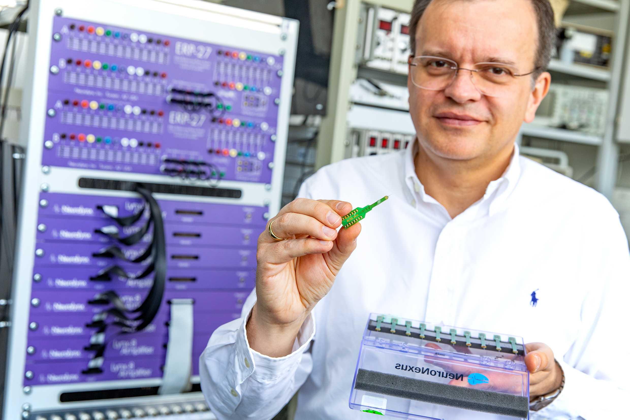 Professor Dr. Andrej Kral steht mit einem Multi-Elektroden-Array in der Hand vor einem Verstärker zur Hirnstrommessung.