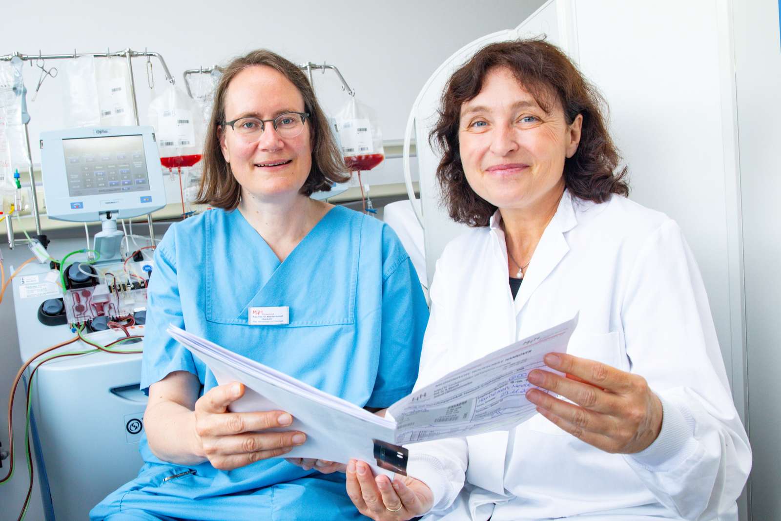 Professor Dr Maecker-Kolhoff (left) and Professor Dr Britta Eiz-Vesper sit in the Institute for Transfusion Medicine and hold a patient file in their hands. Copyright: Karin Kaiser / MHH