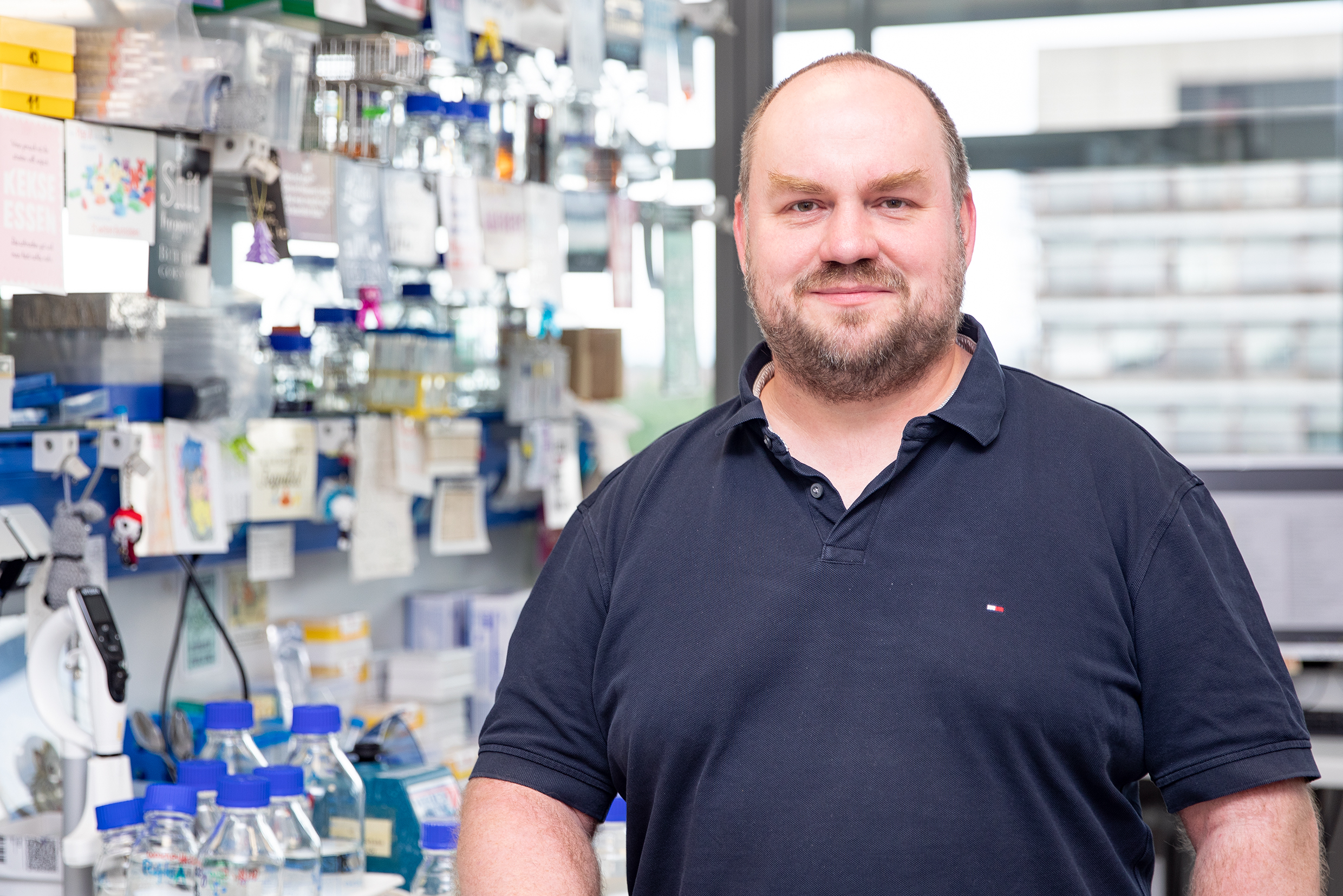 Porträtbild von Christoph Garbers, der in einem Laborraum mit verschiedenen Geräten im Hintergrund steht. 