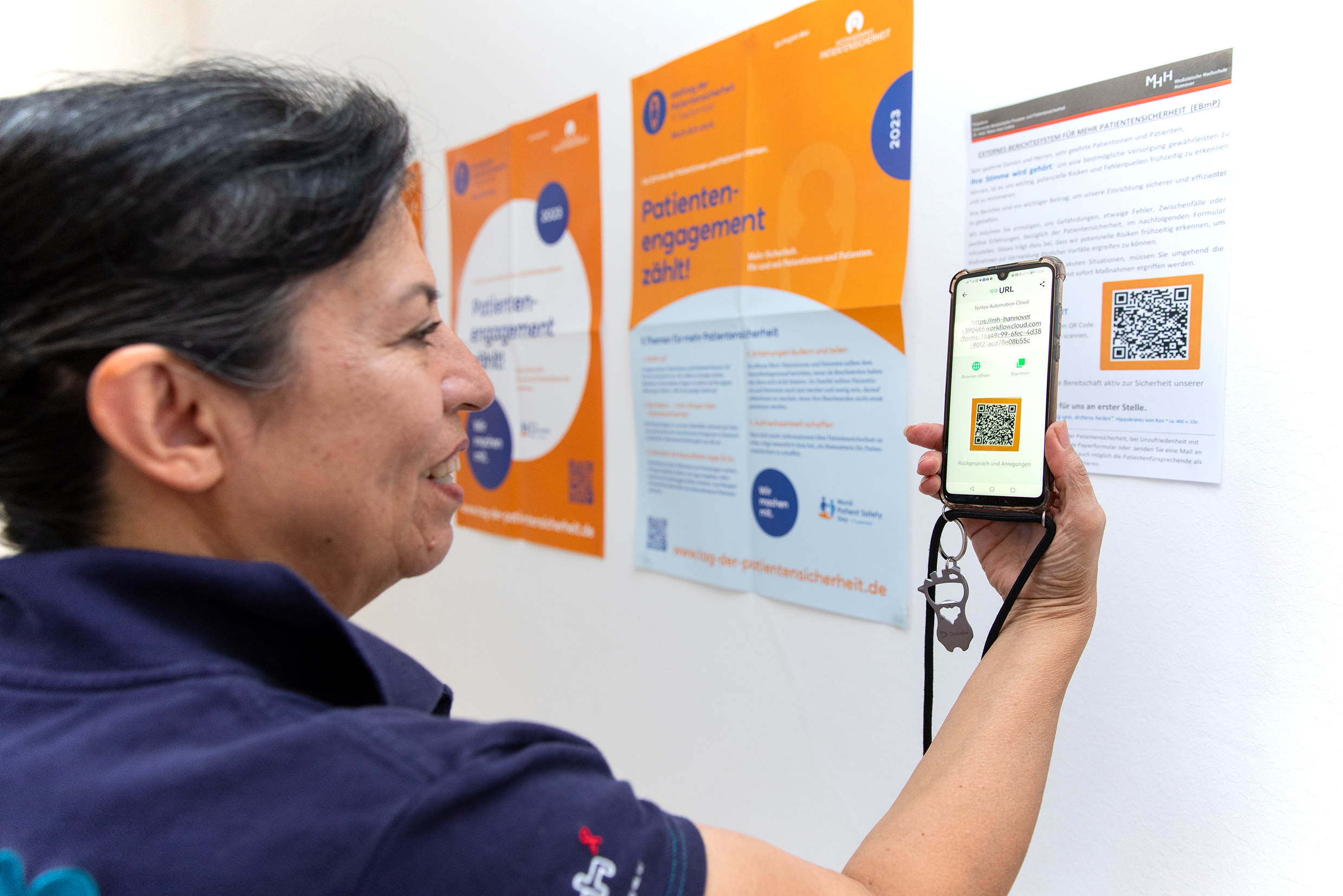 Copyright: Karin Kaiser / MHH Dr. Maria Ines Cartes steht vor einem Poster mit einem QR-Code. Diesen scannt sie mit ihrem Smartphone.