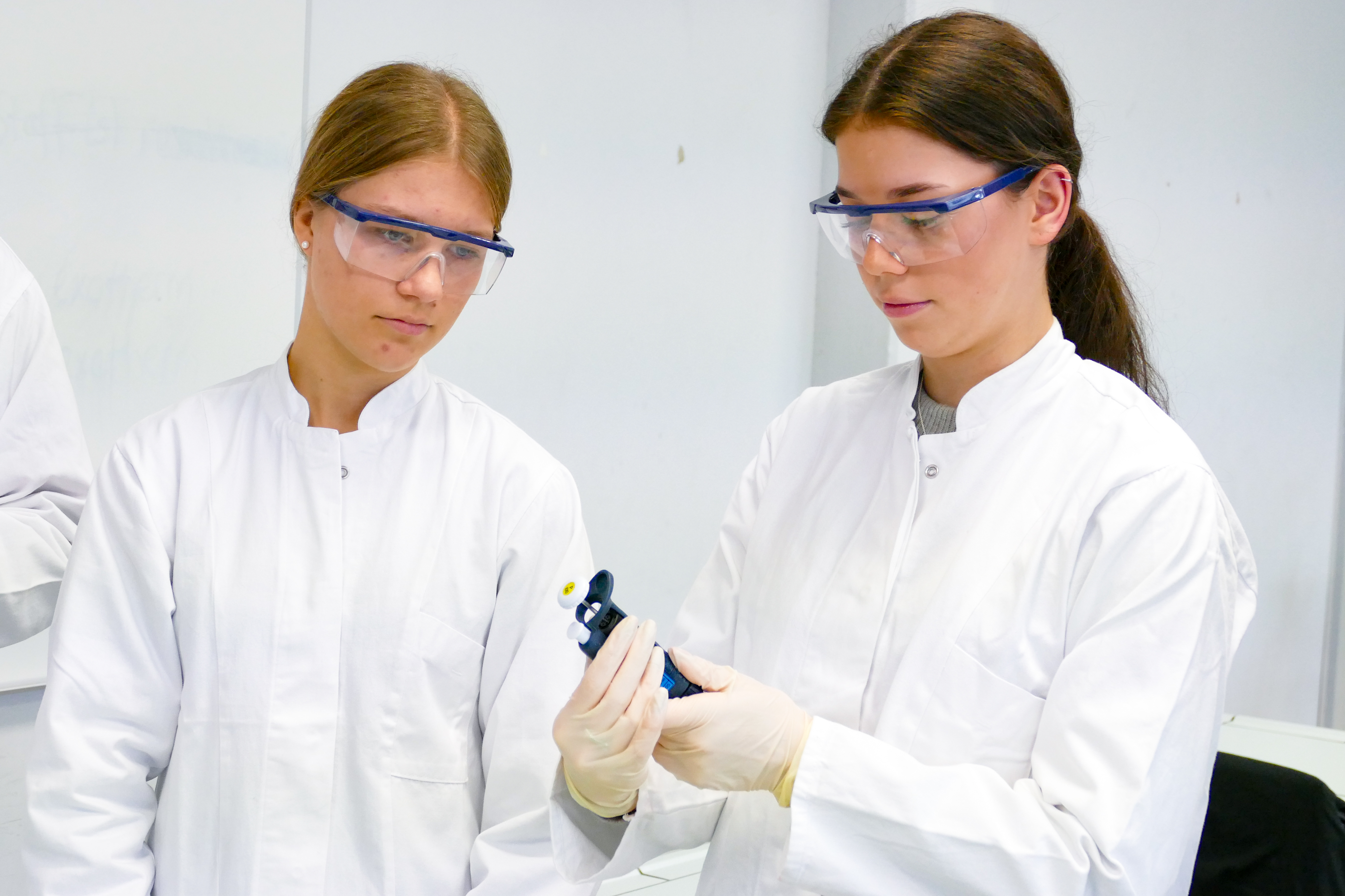 zwei Frauen in weißem Kittel, eine hält ein Objekt in der Hand, die andere schaut dieses an