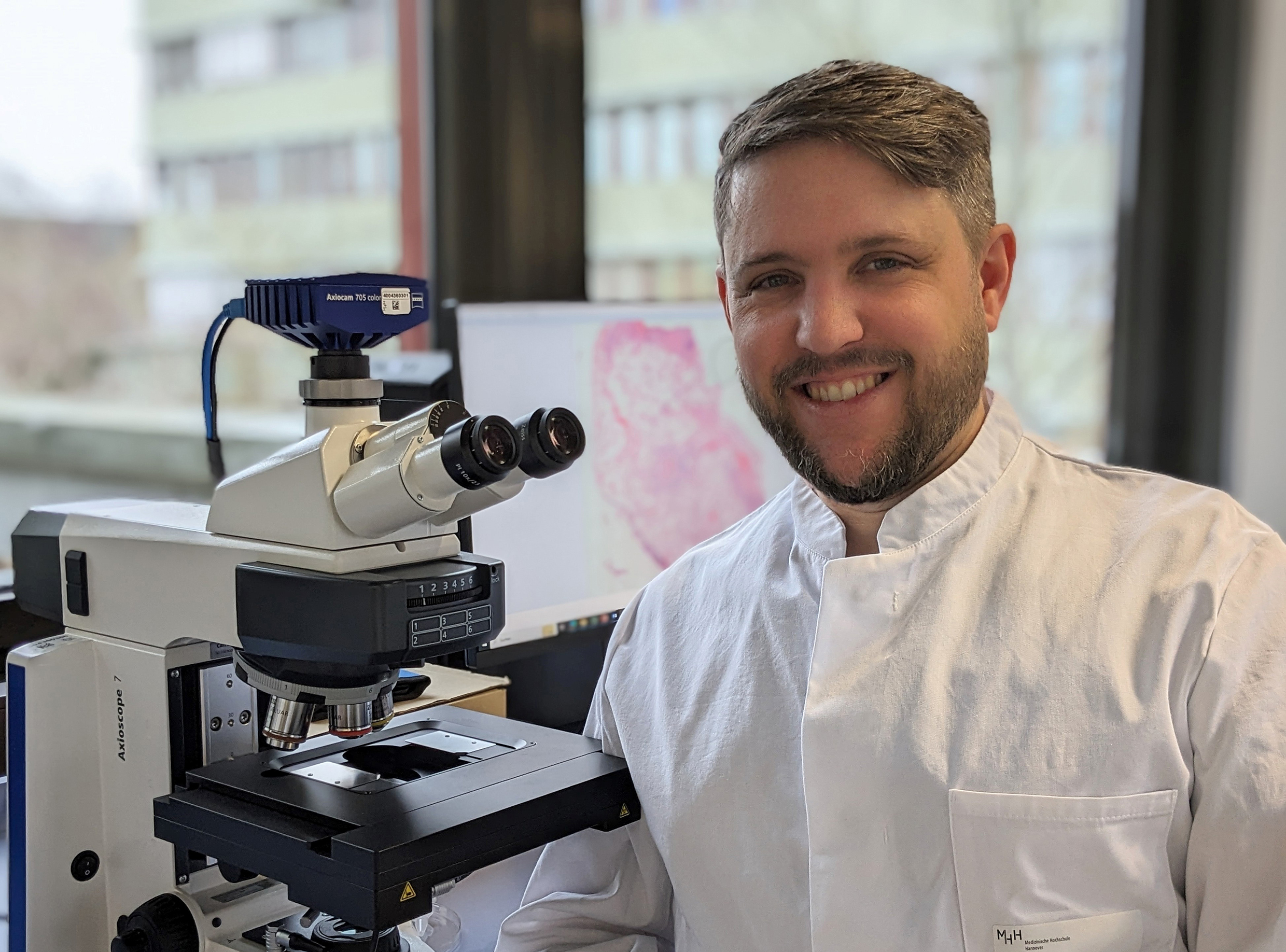 Dr. Jonas Schupp sitzt neben einem Mikroskop. 