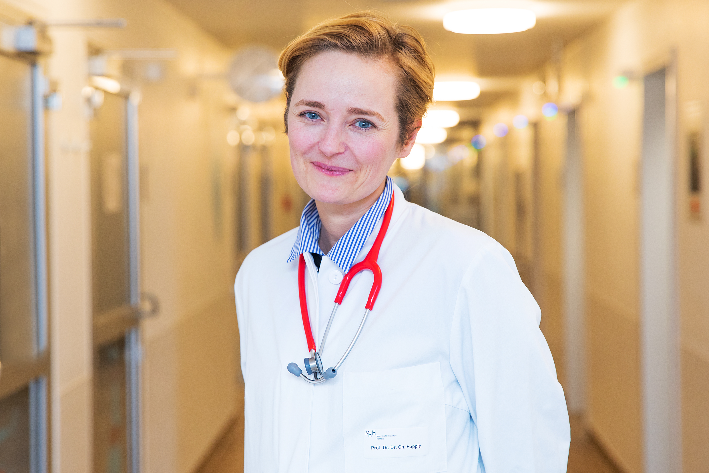 Porträtbild von Prof. Dr. med. Christine Happle, die in weißem Arztkittel in einem Stationsflur steht.