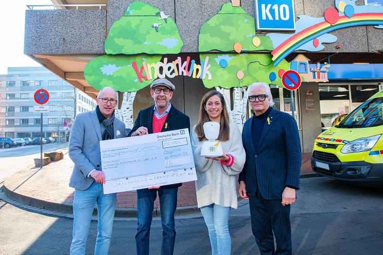 Frederike Ludwig-Lück, Peter Klein, Nils Meyer und Jörg Henschel stehen vor dem Haupteingang der MHH-Kinderklinik und halten eine symbolischen Check in den Händen sowie einen der Avatare, die mit dem Geld finanziert werden. 