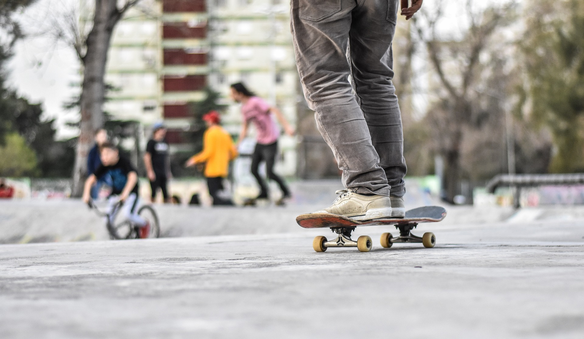 Auf dem Bild sieht man eine Person auf einem Skateboard. Im Hintergrund sind Jugendliche zu sehen. 