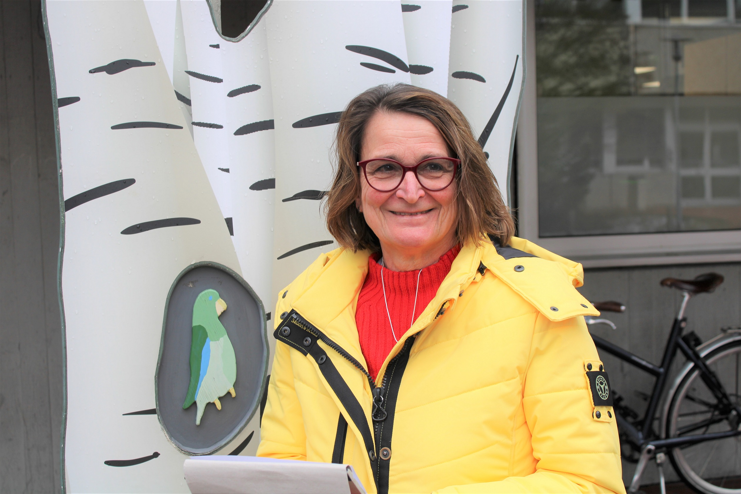 Kirsten Mischke steht in einer gelben Jacke vor einem Gebäude und lächelt in die Kamera.