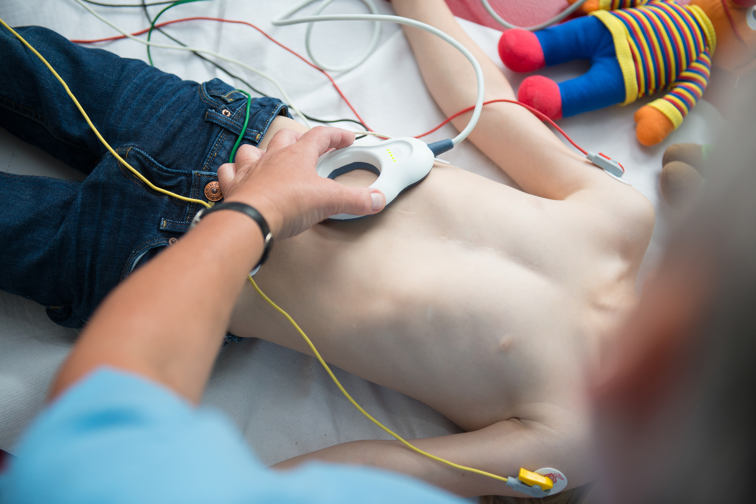 Verkabelter Oberkörper eines Jungen im Bett. Der Junge wird von einer Ärztin untersucht.