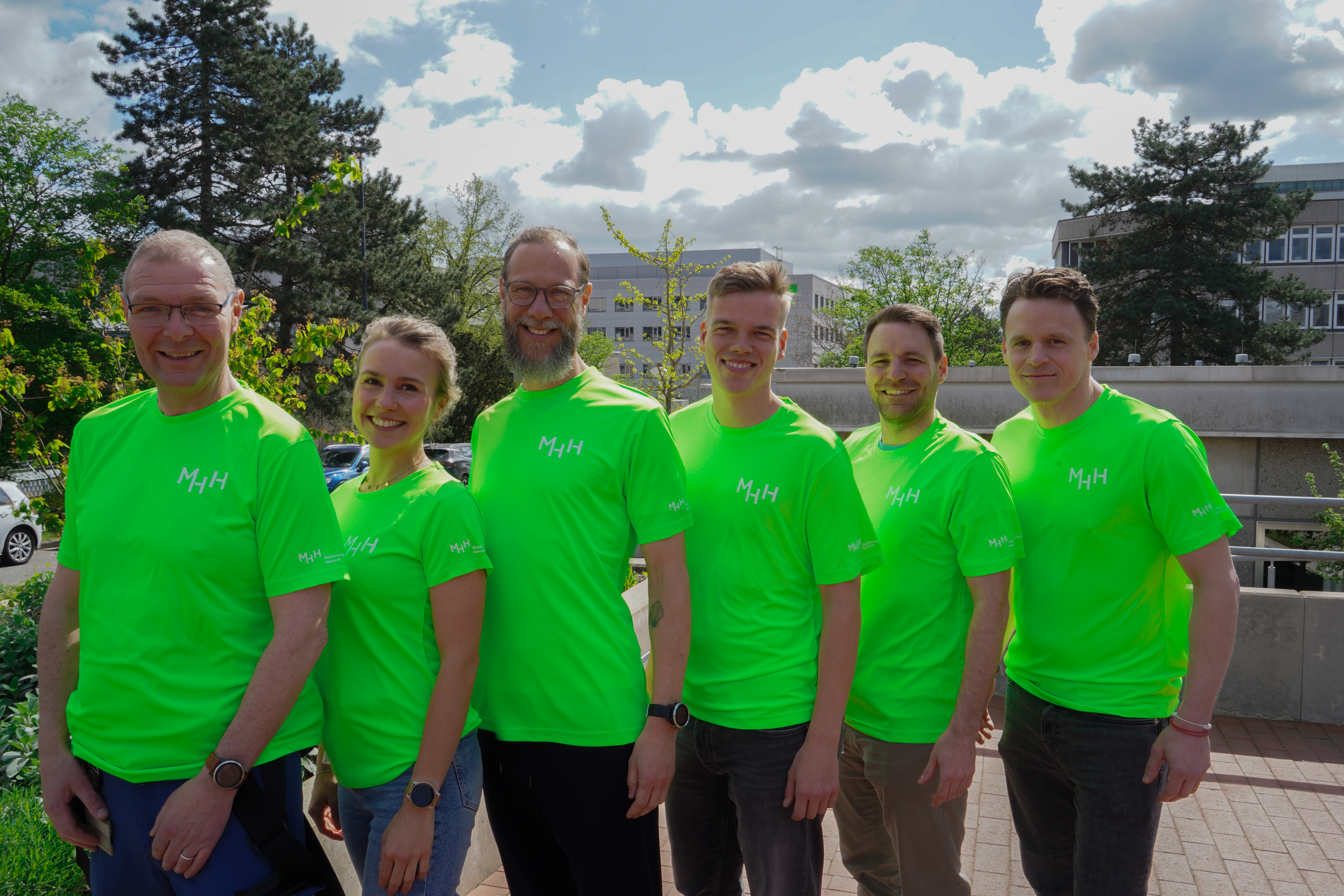 6 Menschen in leuchtend grünen Sport-Shirts mit weißem MHH-Aufdruck auf der Brust und dem Ärmel