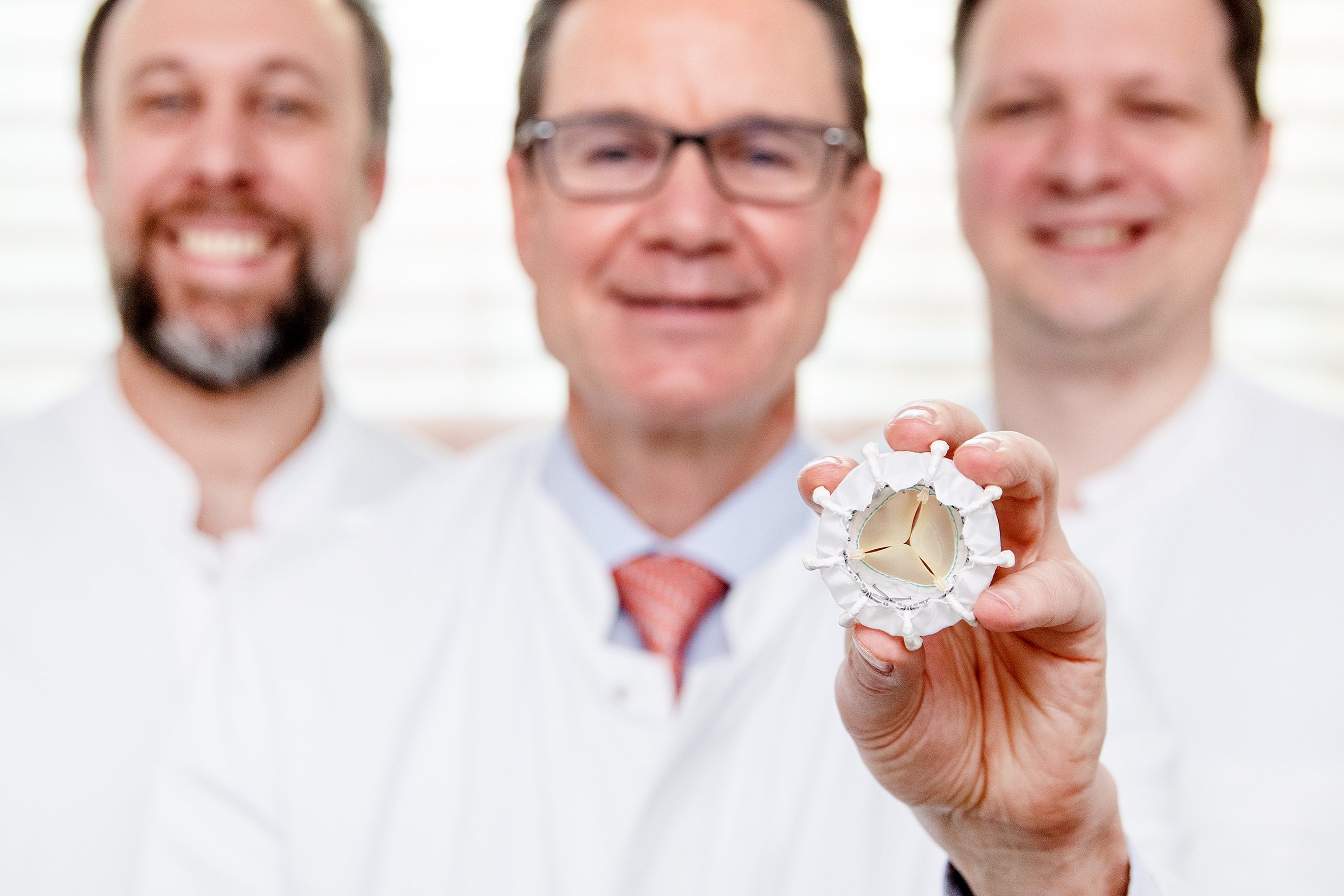 Three doctors in white coats, one holding the new prosthesis for the tricuspid valve.