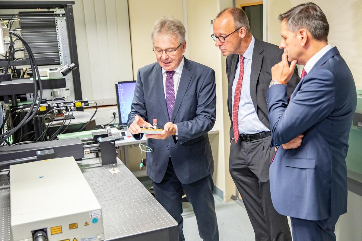 Professor Reinhold Förster zeigt Bundeskanzler Friedrich Merz und Ministerpräsident Olaf Lies einen Probenbehälter.