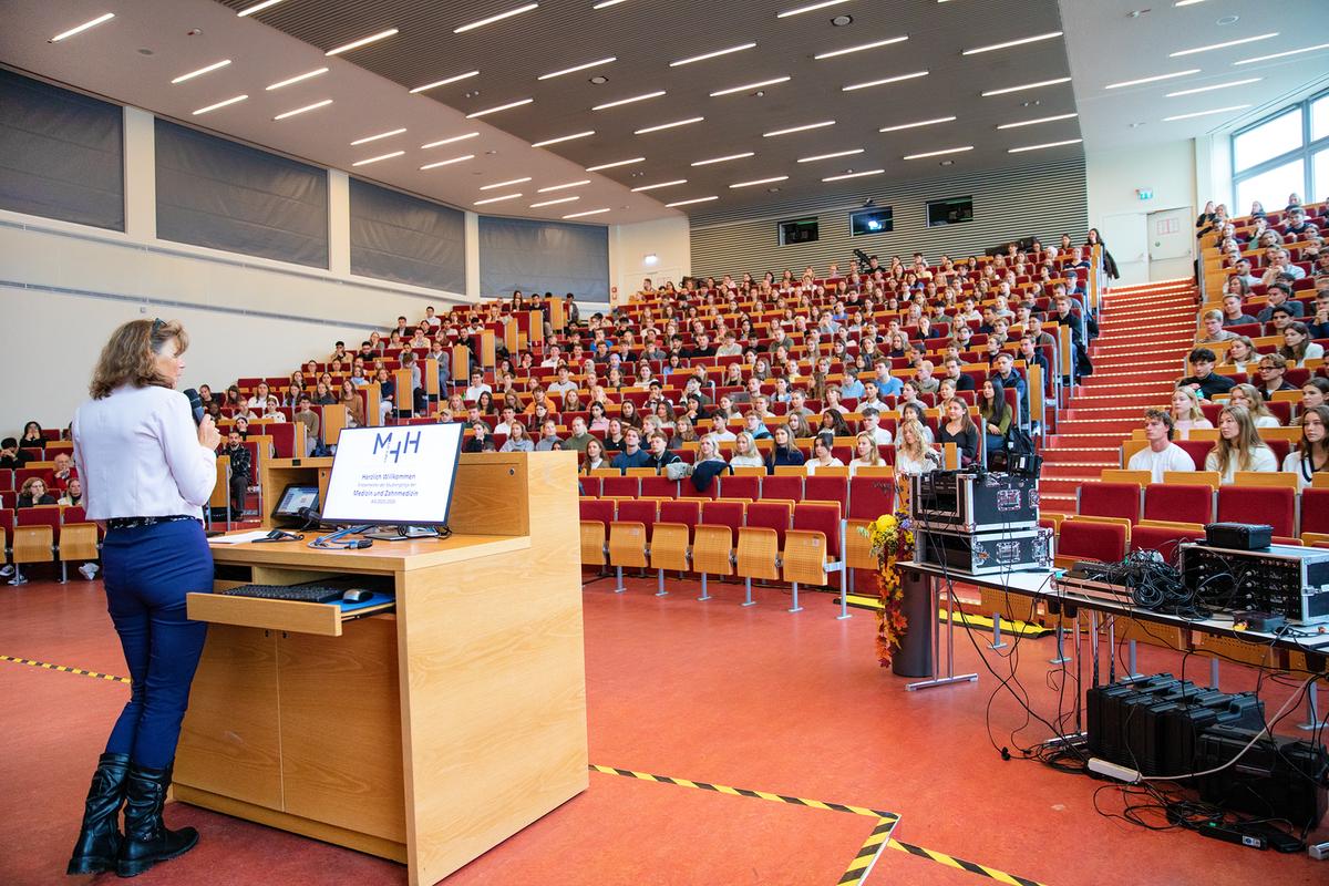 View from the lectern into a packed lecture hall. On the left stands MHH President Denise Hilfiker-Kleiner, addressing the first-year students.
