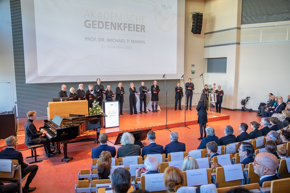 Im Hörsaal F der MHH steht auf dem Podium der MHH-Chor, daneben ein Mann am Klavier, in den Sitzreihen sitzen viele Menschen. 