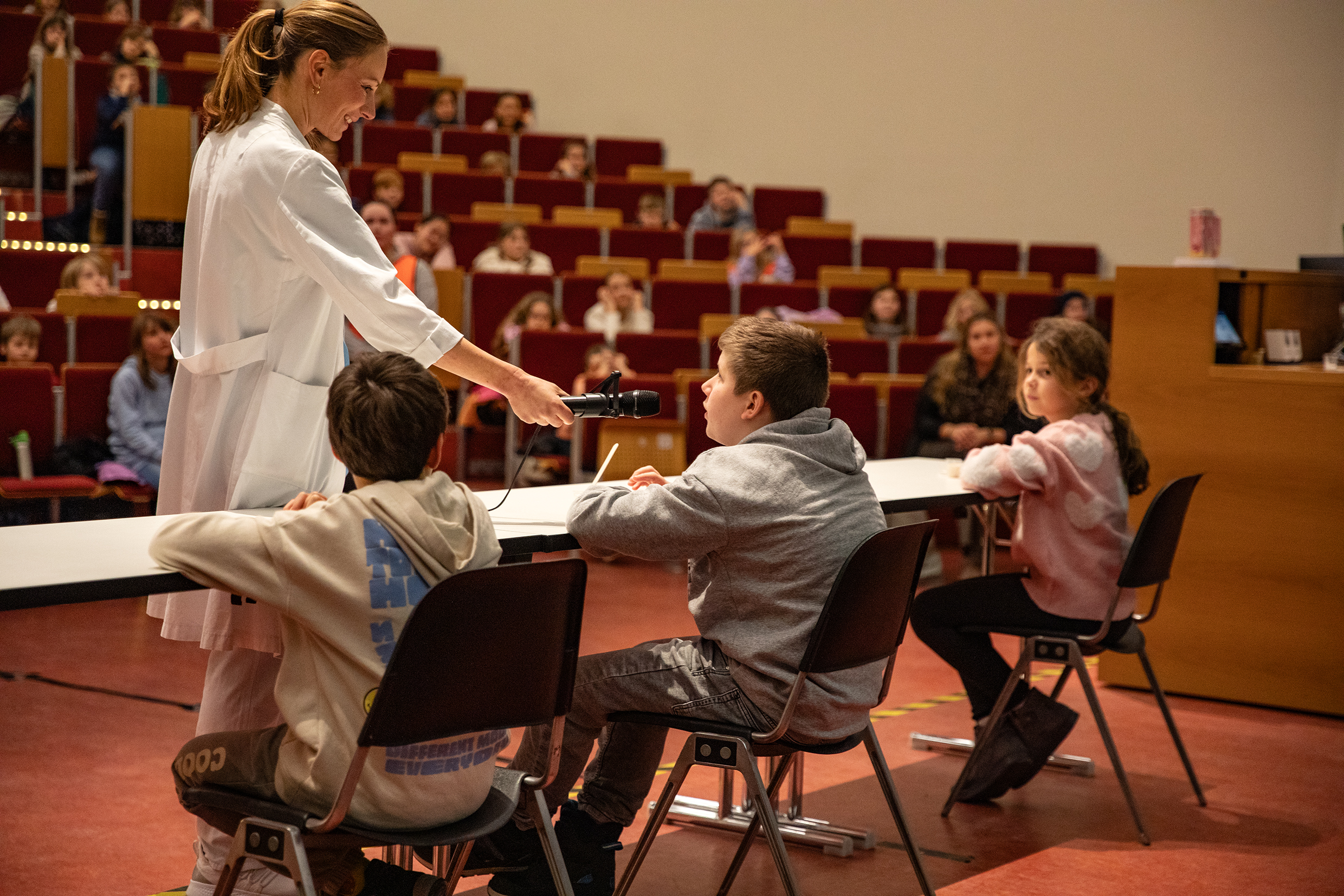 Dr. Eva Moennig hält einem Jungen während der Vorlesung im Hörsaal ein Mikrofon hin. 