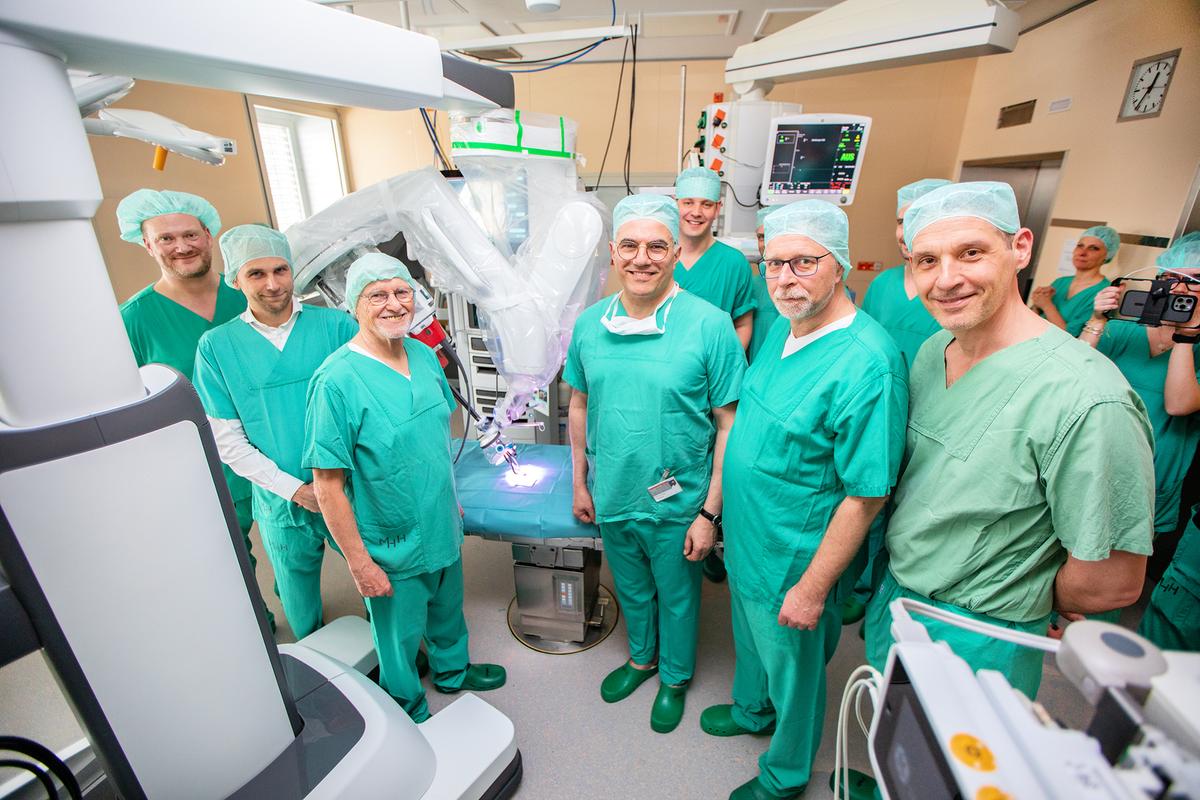 A group of men in surgical scrubs is standing next to a surgical robot. 