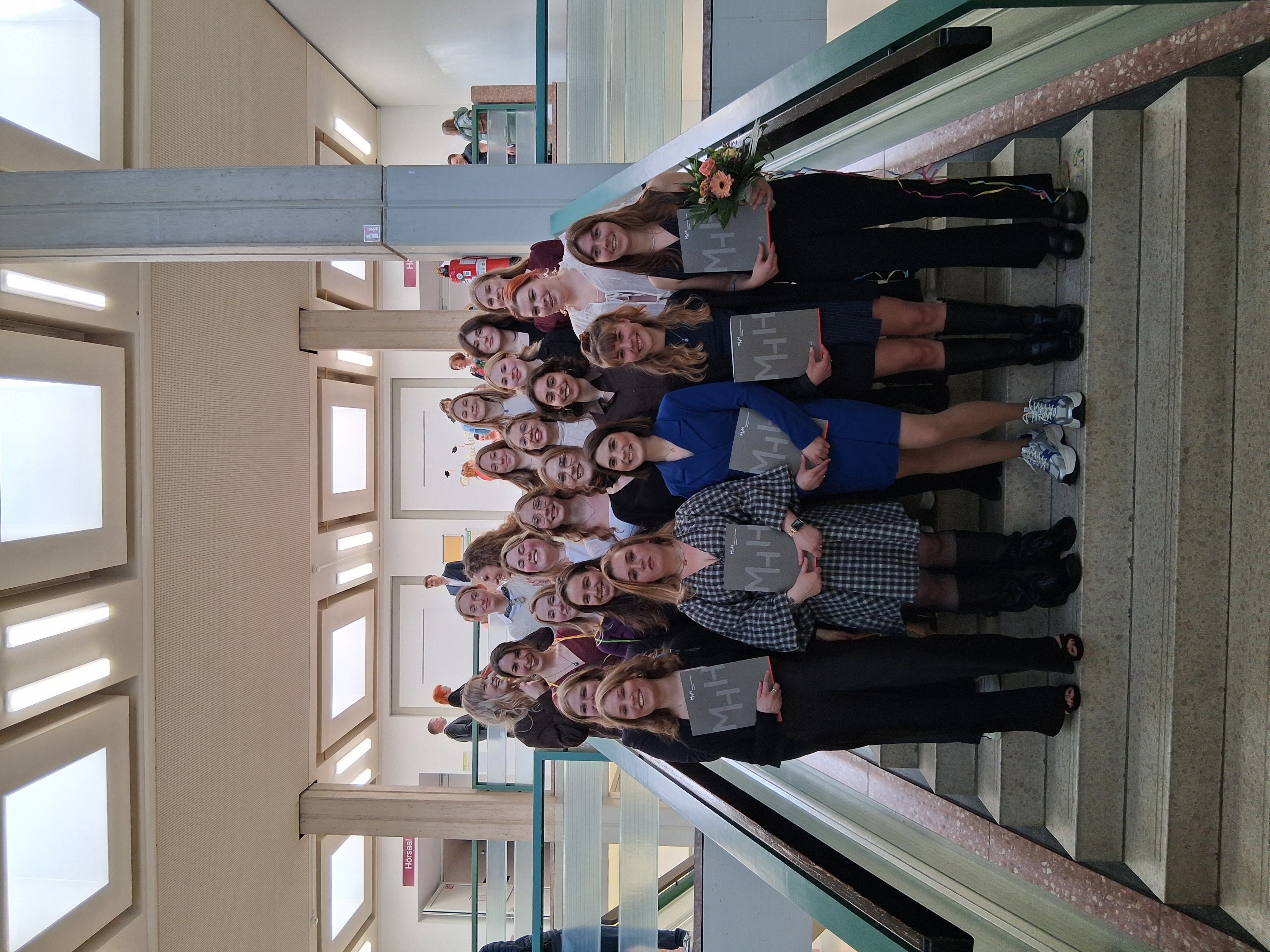 Die Absolventinnen stehen für ein Gruppenfoto auf einer Treppe zusammen. 