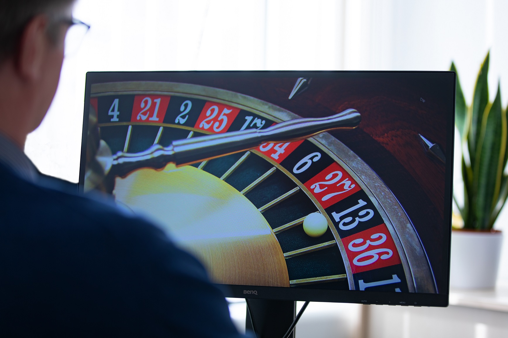 Ein Mann sitzt vor einem PC-Monitor, auf dem ein virtuelles Roulettespiel zu sehen ist. 