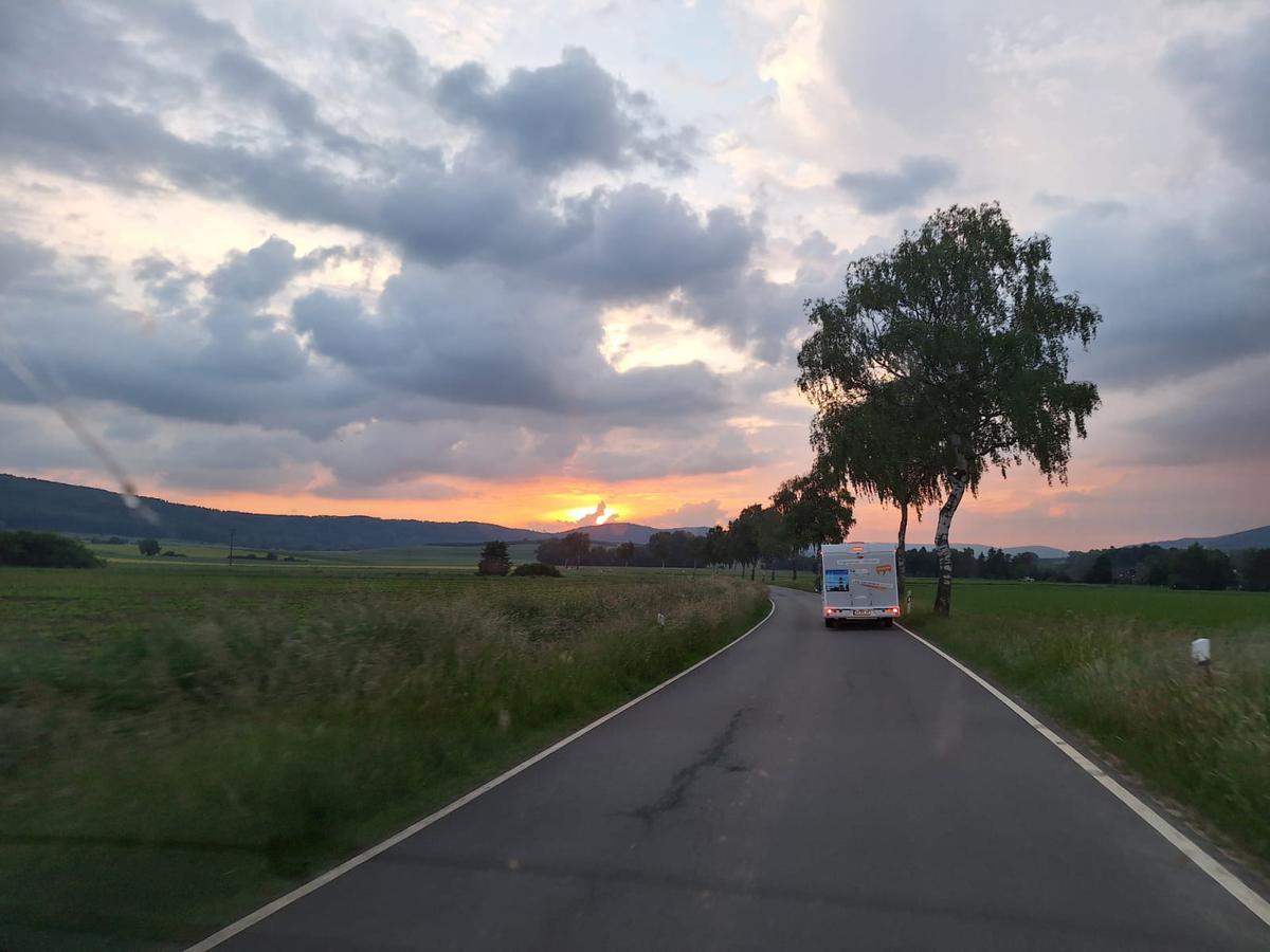 Ein Organspende-Campervan fährt auf einer leeren Landstraße. Am Himmel zeichnet sich ein Regenbogen ab.