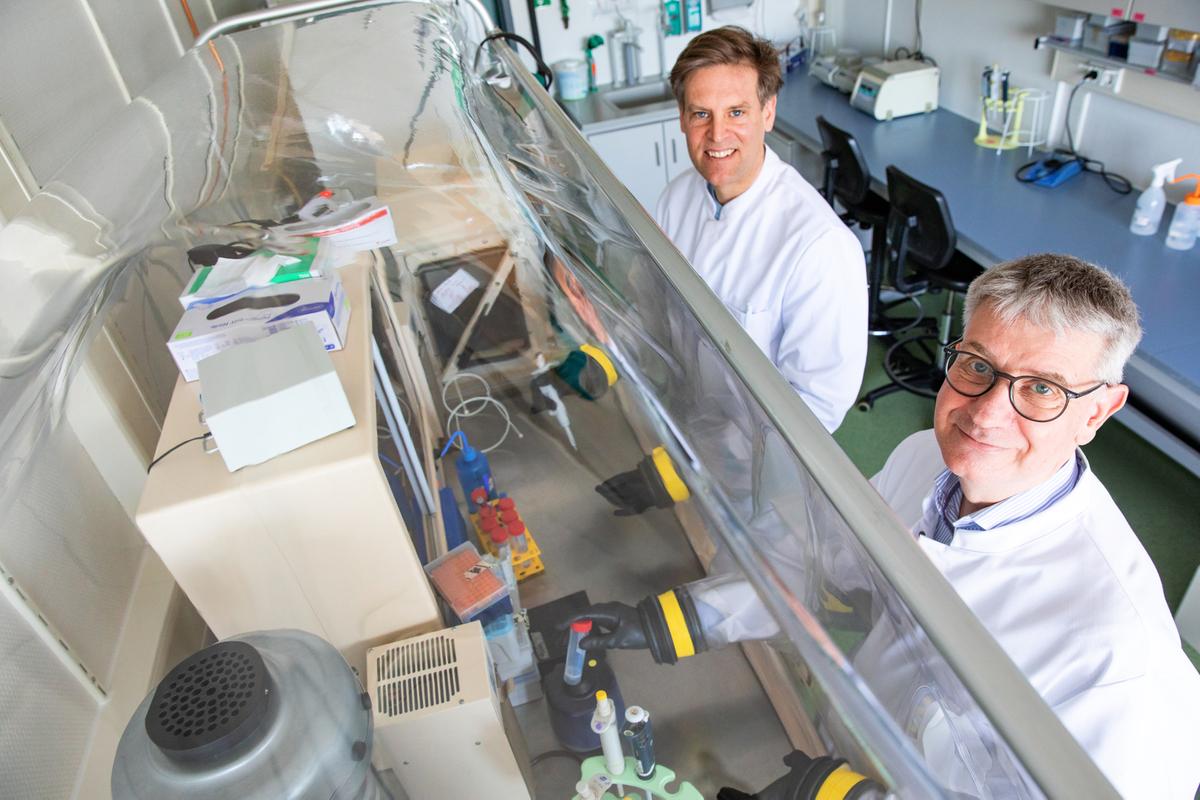 Two men in white lab coats are standing at a lab bench in a laboratory.