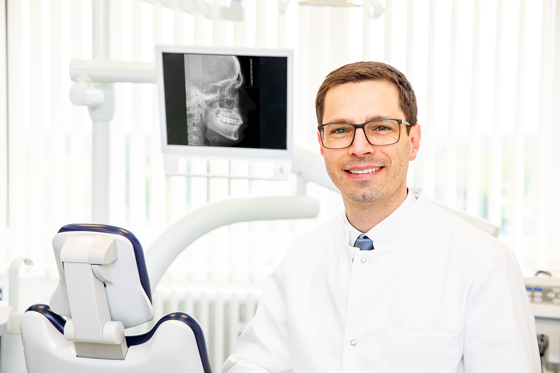 Prof. Kunz stands in front of a dental chair in the Clinical Department of Orthodontics; behind him, a monitor displays an X-ray image. 