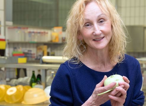 MHH-Ernährungsexpertin Sonja Nothacker sitzt in einer Lehrküche mit einem Kohlrabi in der Hand auf einem Tisch. 