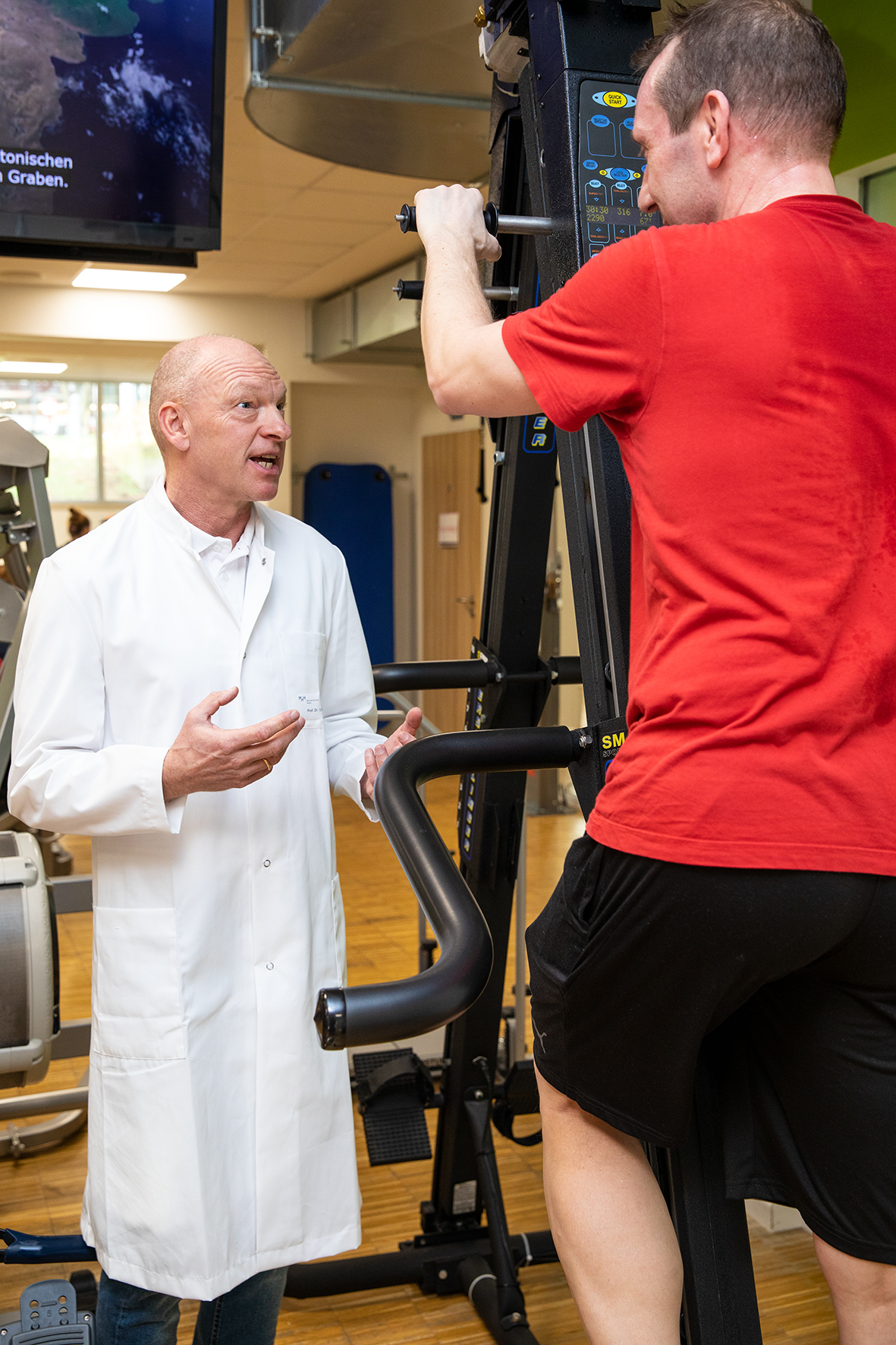 Professor Tegtbur steht neben eine Mann, der auf einem Sportgerät trainiert.  