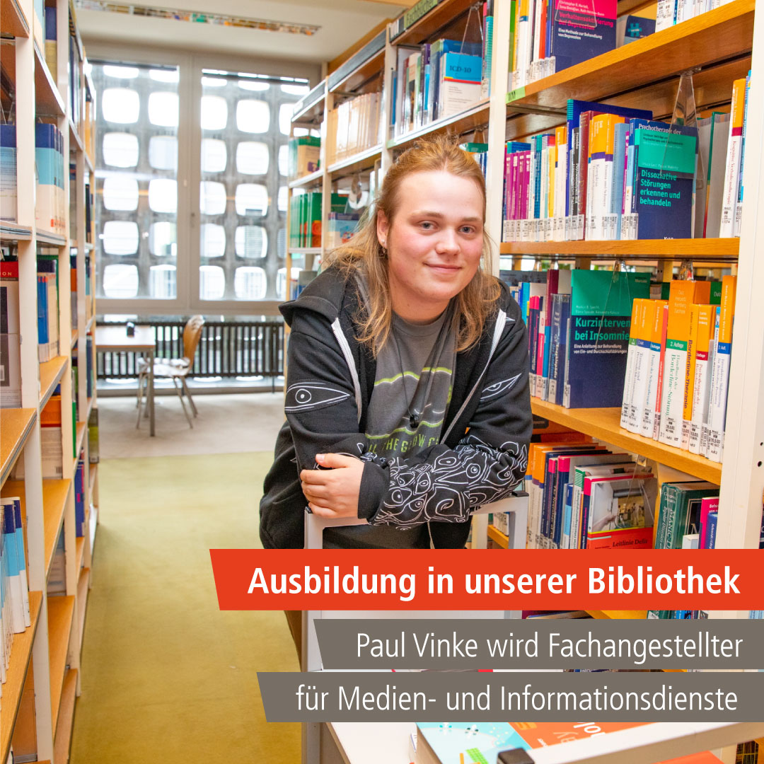 Azubi Paul Vinke steht in der Bibliothek und schaut in die Kamera