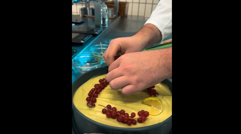 Zwei Hände dekorieren Johannisbeeren auf einem Kuchen.