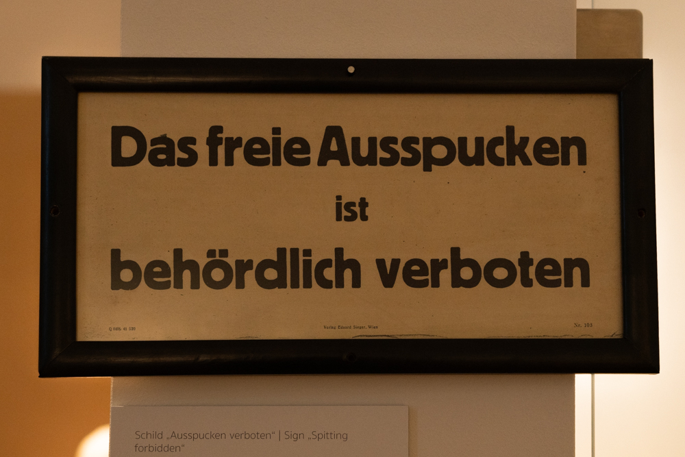 Foto eines Schildes mit der Aufschrift "Das freie Ausspucken ist behördlich verboten."